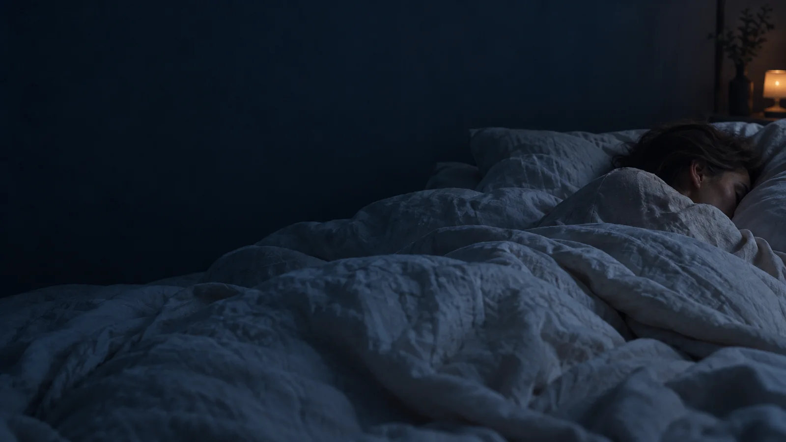 A woman asleep beneath a linen duvet in a softly lit bedroom.